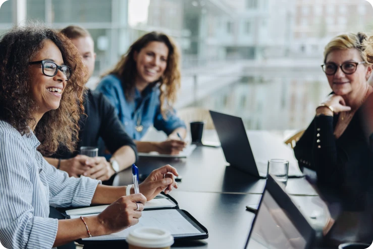 An image of coworkers gathered around a table smiling and discussing